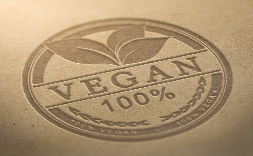 Stempel makanan bersertifikat Vegan dideboss di atas latar belakang alami coklat